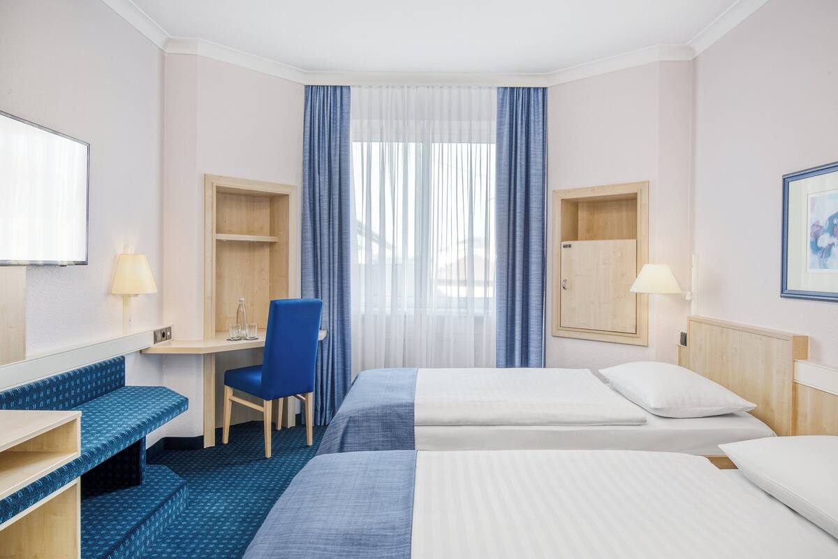 A hotel room with two beds, a desk, a chair, and a TV.