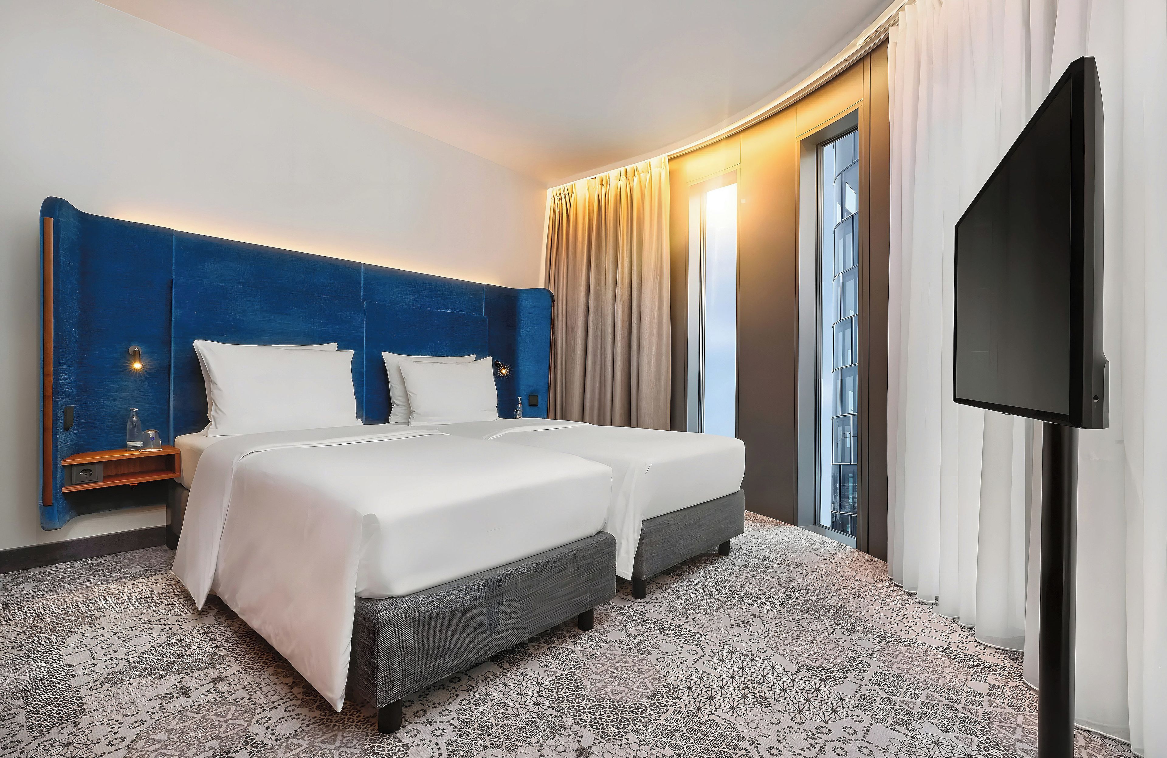 A hotel room with a large bed, a TV, and a window with curtains.