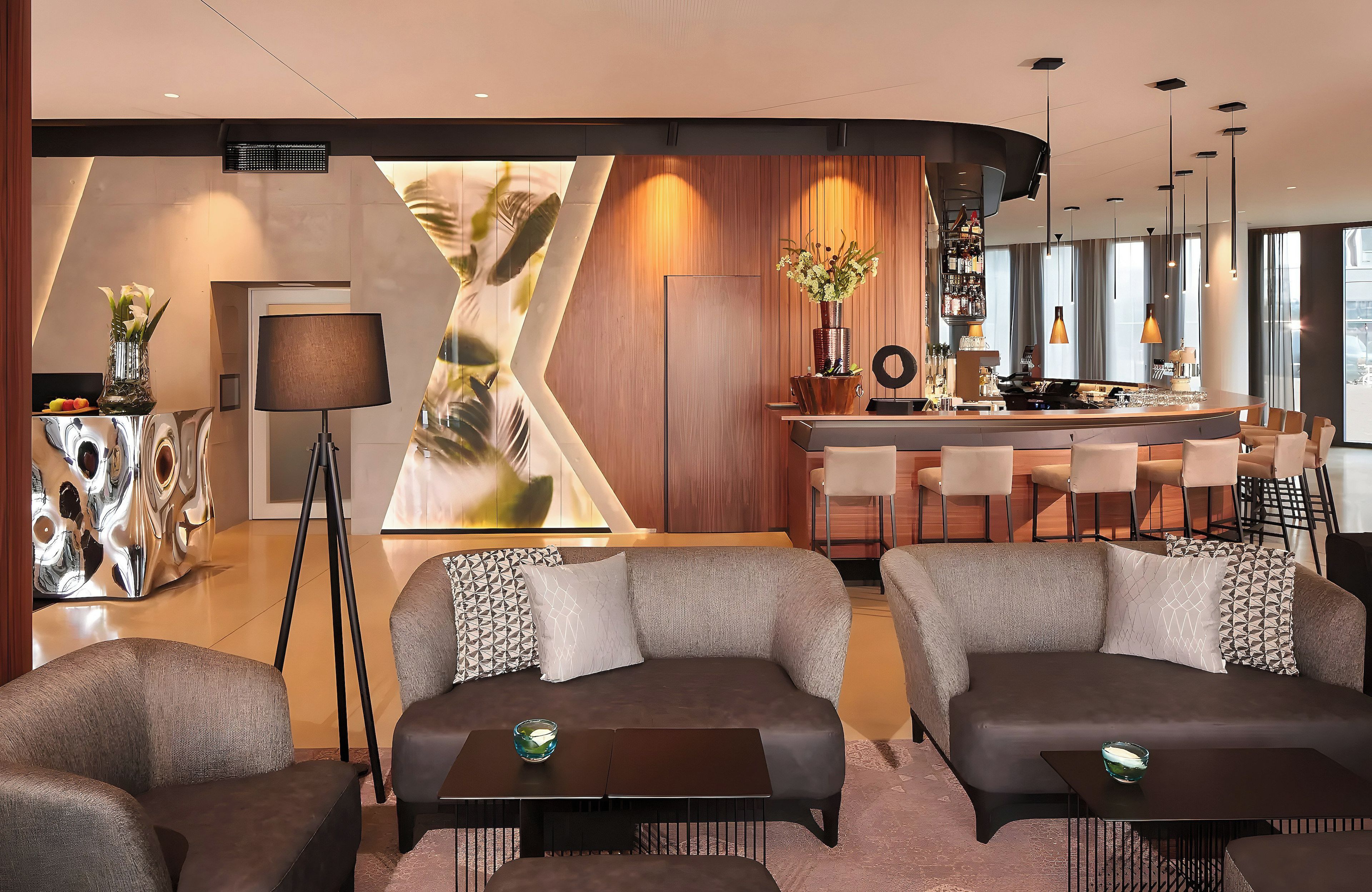 Un hall d’hôtel moderne doté d’un bar, d’espaces aménagés pour s’asseoir et d’une grande œuvre d’art abstraite qui orne un mur.