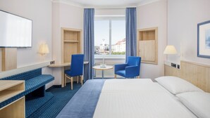Habitación de hotel con cama, dos sillas, una mesita, televisor y ventana con cortinas.