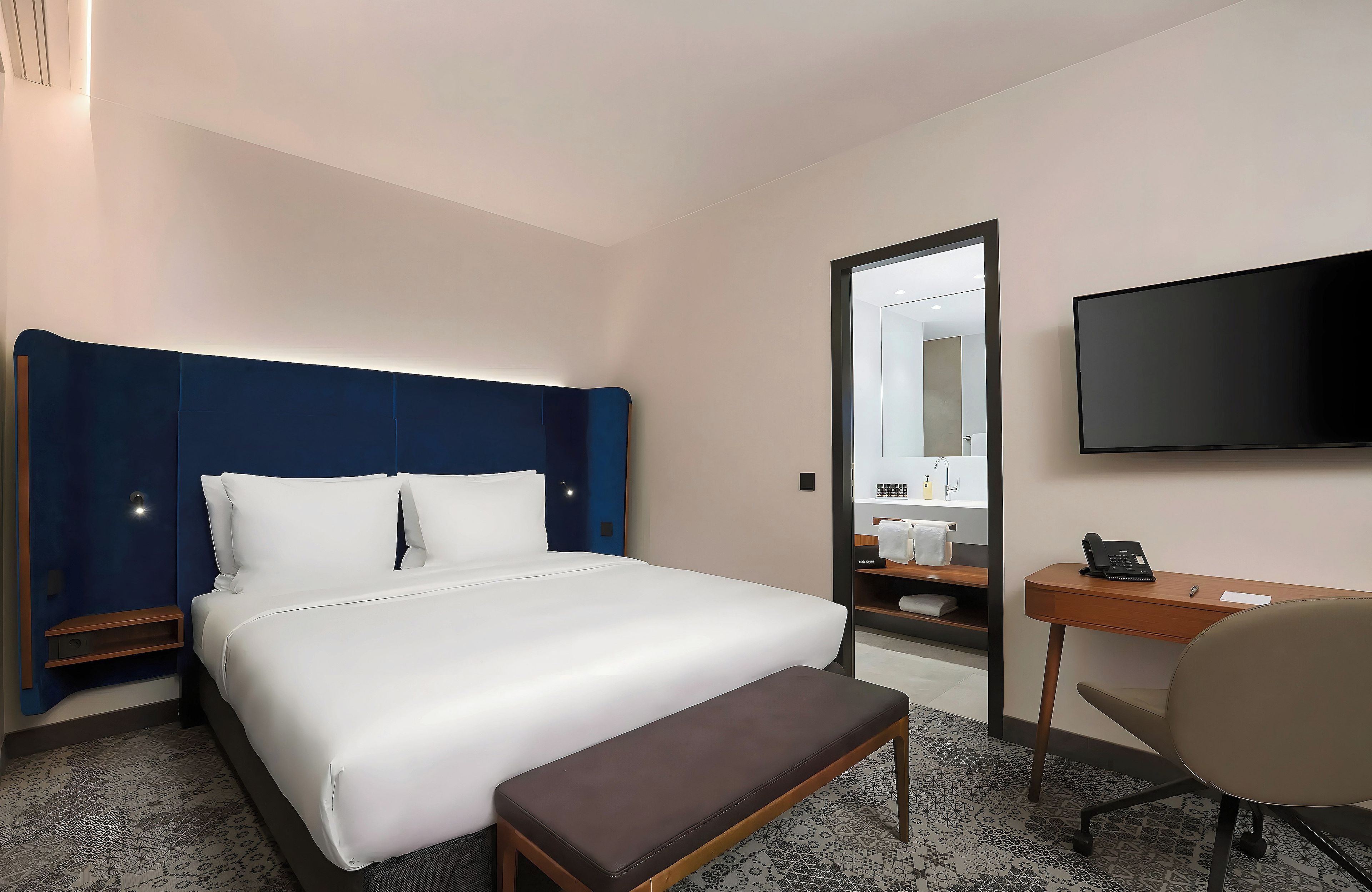 A hotel room with a large bed, a desk, a chair, a television, and a mirror.