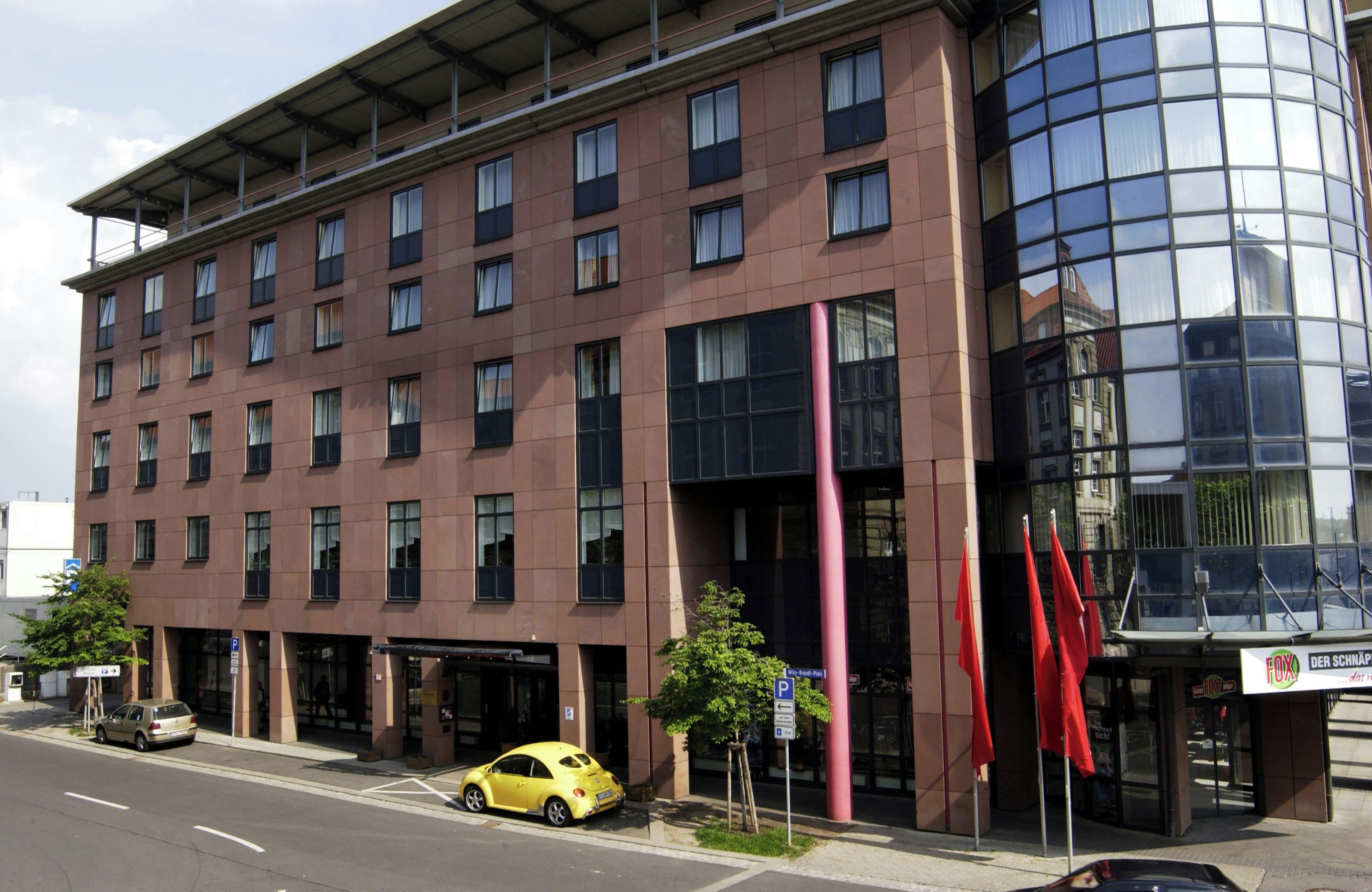 Un edificio de varios pisos con fachada moderna, amplios ventanales y entrada en esquina.