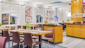 Un comedor moderno con mesas y sillas, una isla central con una exhibición de frutas y una cocina con armarios y mostrador.