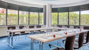 Un salón de conferencias con una larga mesa, sillas y amplios ventanales que dan a vistas de árboles y edificios.