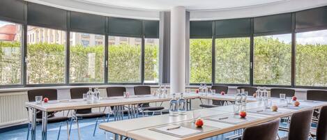 Un salón de conferencias con una larga mesa, sillas y amplios ventanales que dan a vistas de árboles y edificios.