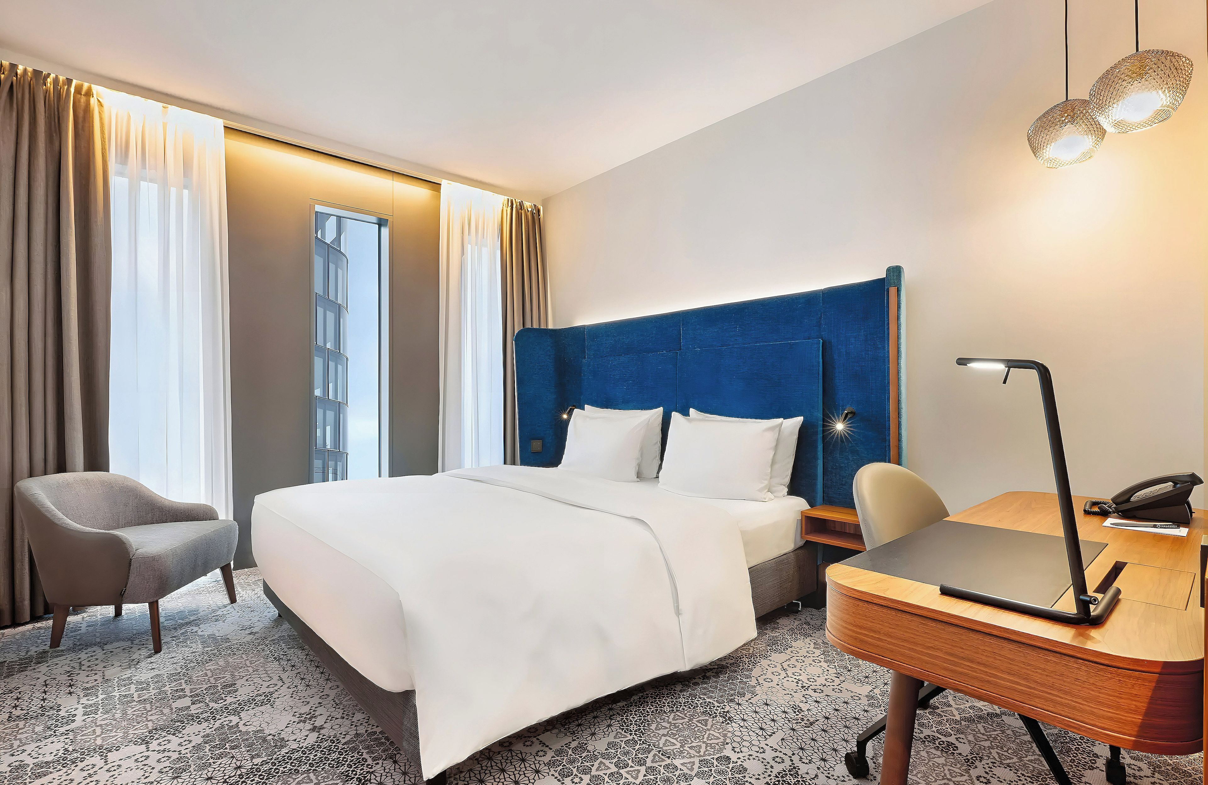 Une chambre d’hôtel avec un lit, un bureau, une chaise et un téléphone.