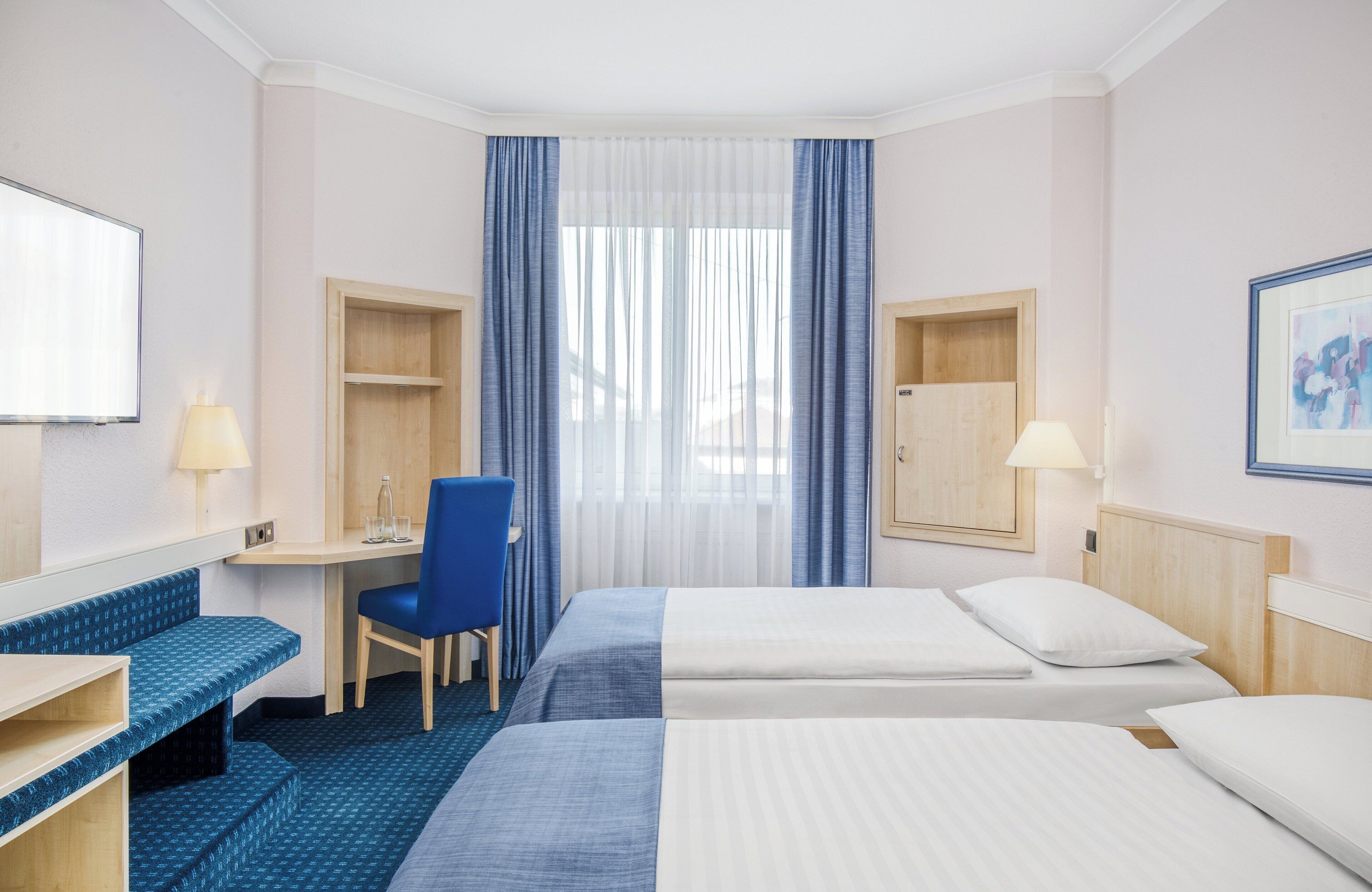 Habitación de hotel con dos camas, un escritorio, una silla y un televisor.