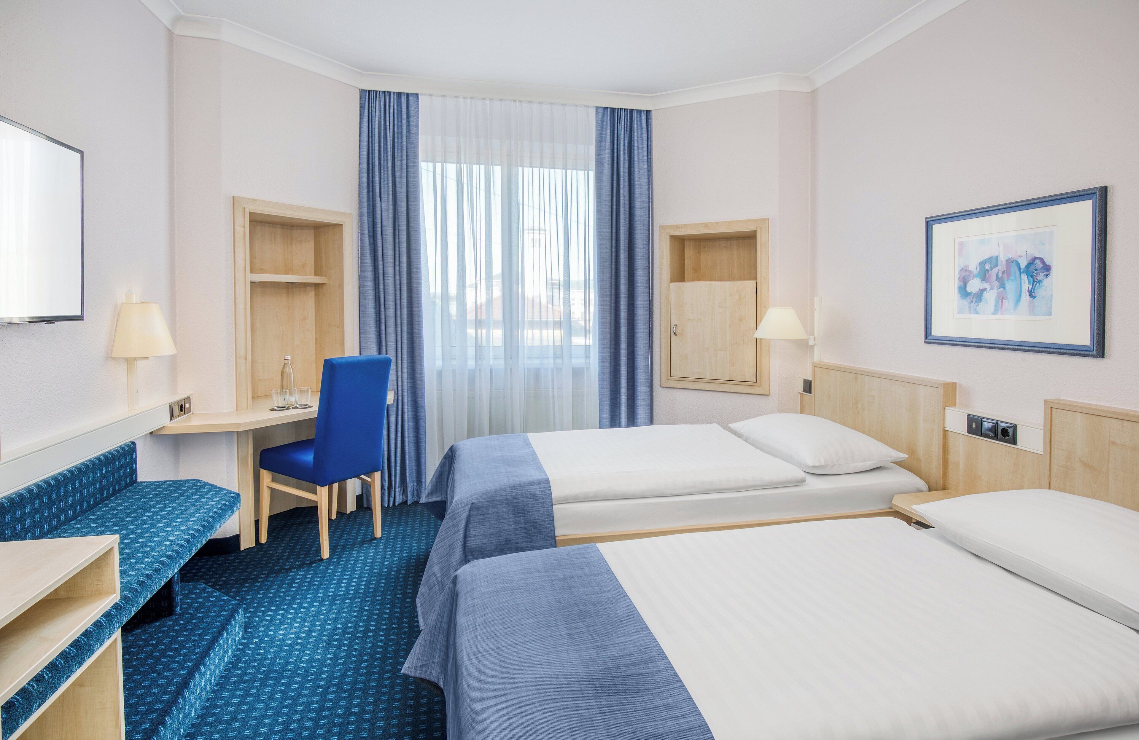 A hotel room with two beds, a desk, a chair, and a small seating area.