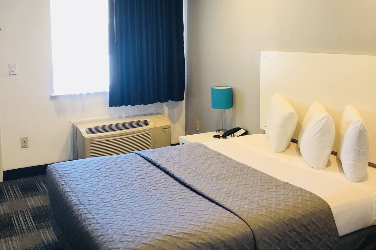 A hotel room with a bed, a nightstand, a lamp, and a window with curtains.