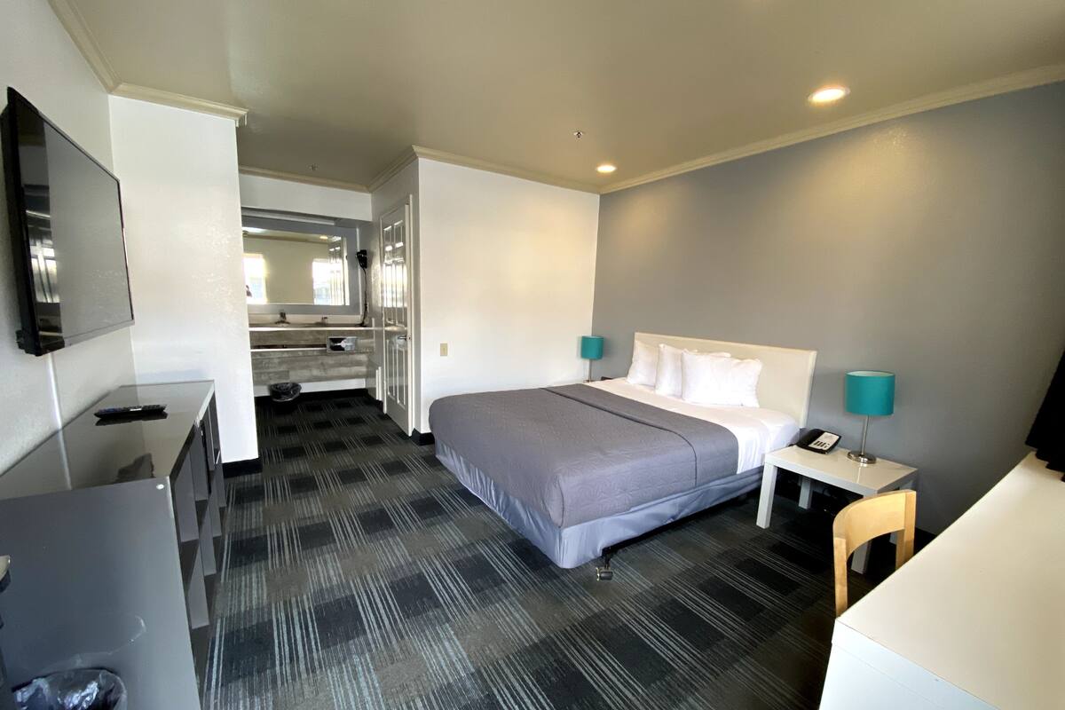 A hotel room with a bed, bedside tables, a desk, a mirror, and a television.