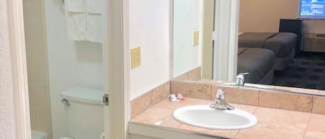 Un bagno d'albergo con il water bianco, un lavandino con specchio e una zona doccia.