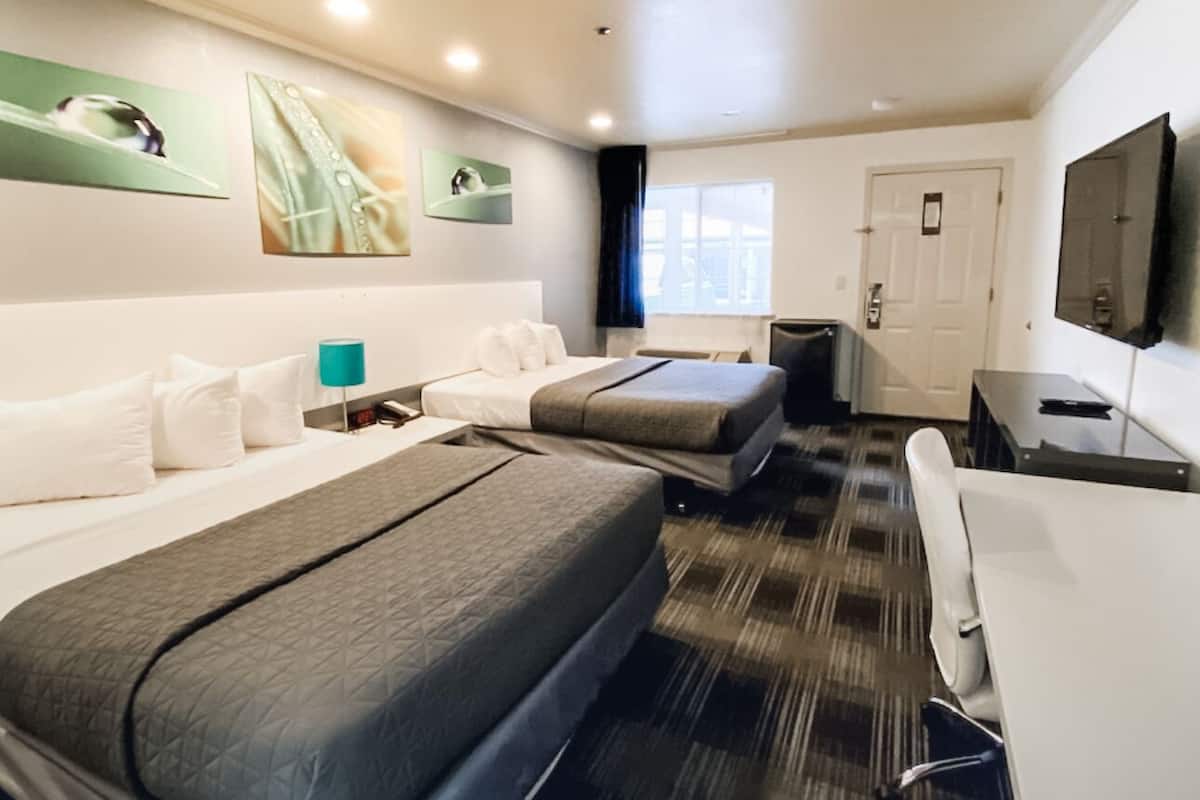 A hotel room with two beds, a desk, a chair, a TV, and artwork on the walls.