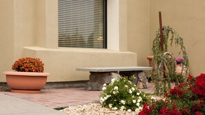 A patio area with a stone bench, a potted plant with orange flowers, and a variety of potted plants with red and white flowers. - Mountain Home Inn (Mountain Home)