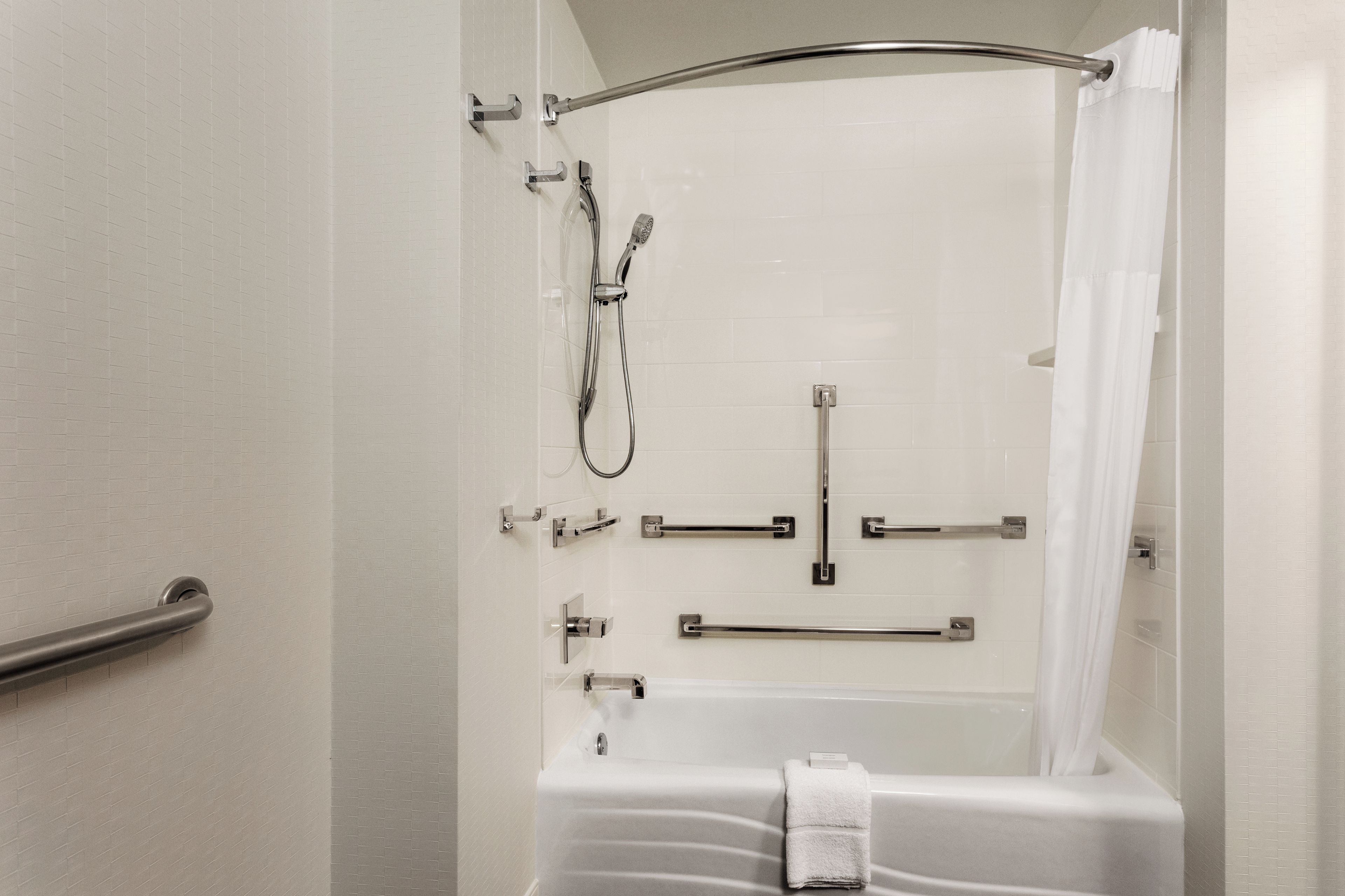 A bathroom with a shower, grab bars, and a towel rack.