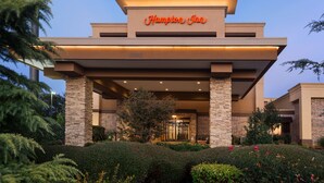 Un hotel Hampton Inn con diseño moderno, que presenta fachada de piedra y un jardín bien cuidado con diversas plantas y flores.