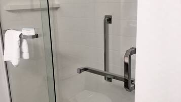 A glass-enclosed shower with a white tiled wall, a towel rack, and a grab bar.