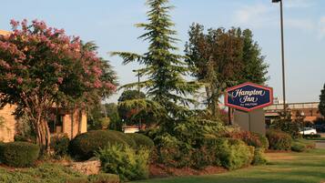 A landscaped area with a sign for Hampton Inn by Hilton, surrounded by well-maintained bushes and trees.