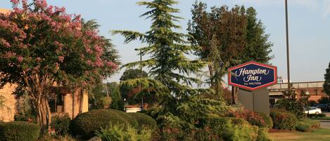 A landscaped area with a sign for Hampton Inn by Hilton, surrounded by well-maintained bushes and trees.
