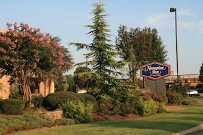 A landscaped area with a sign for Hampton Inn by Hilton, surrounded by well-maintained bushes and trees.