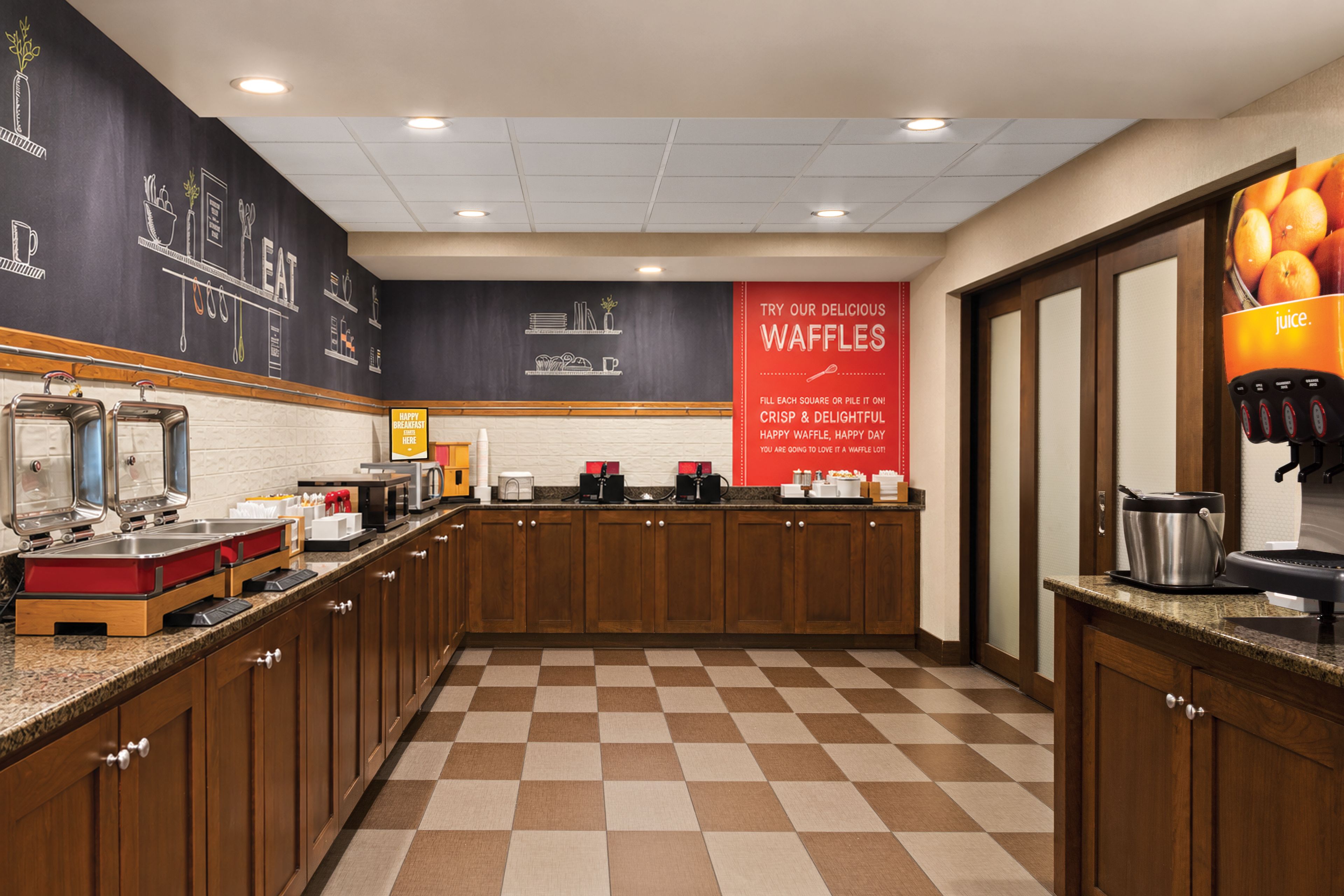 Un área de cocina con piso a cuadros, armarios de madera y un banner rojo que anuncia gofres.
