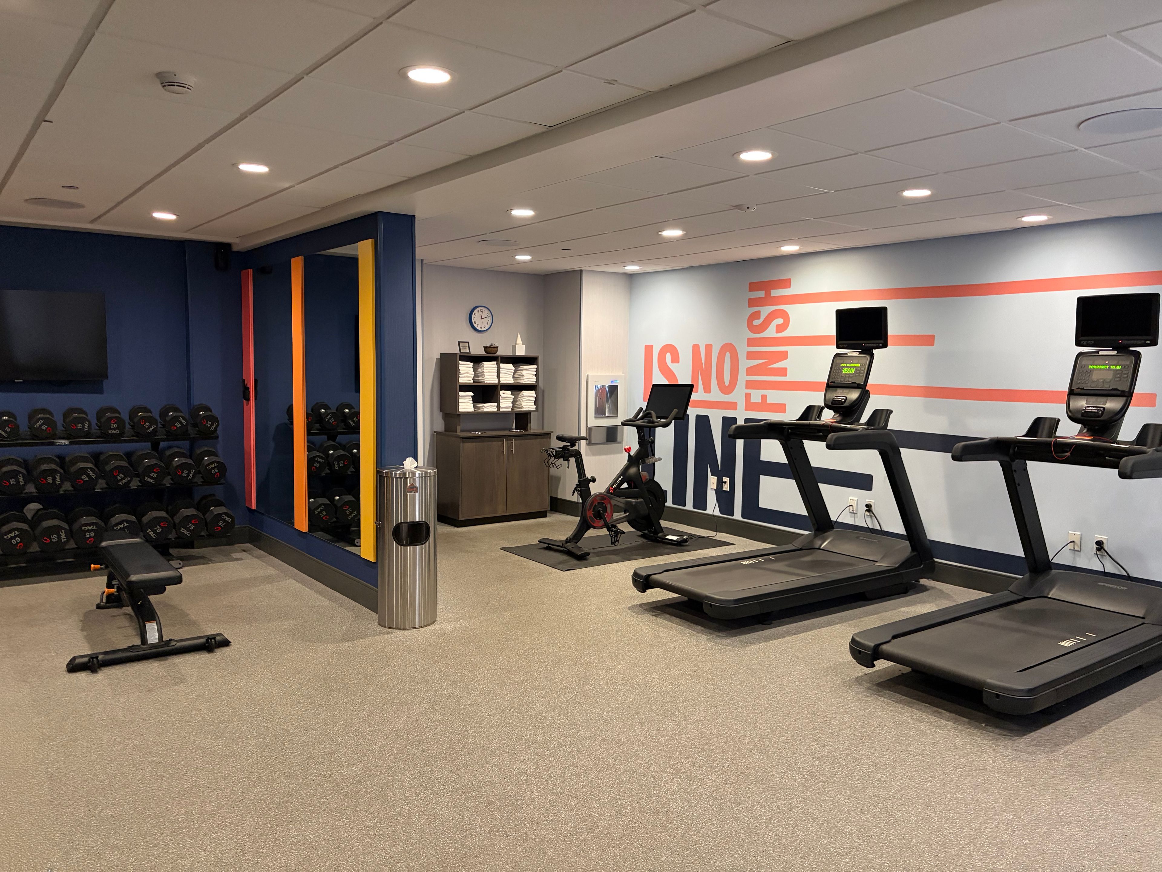 Un gimnasio con cintas de correr, mancuernas y una pared con mensajes motivacionales.