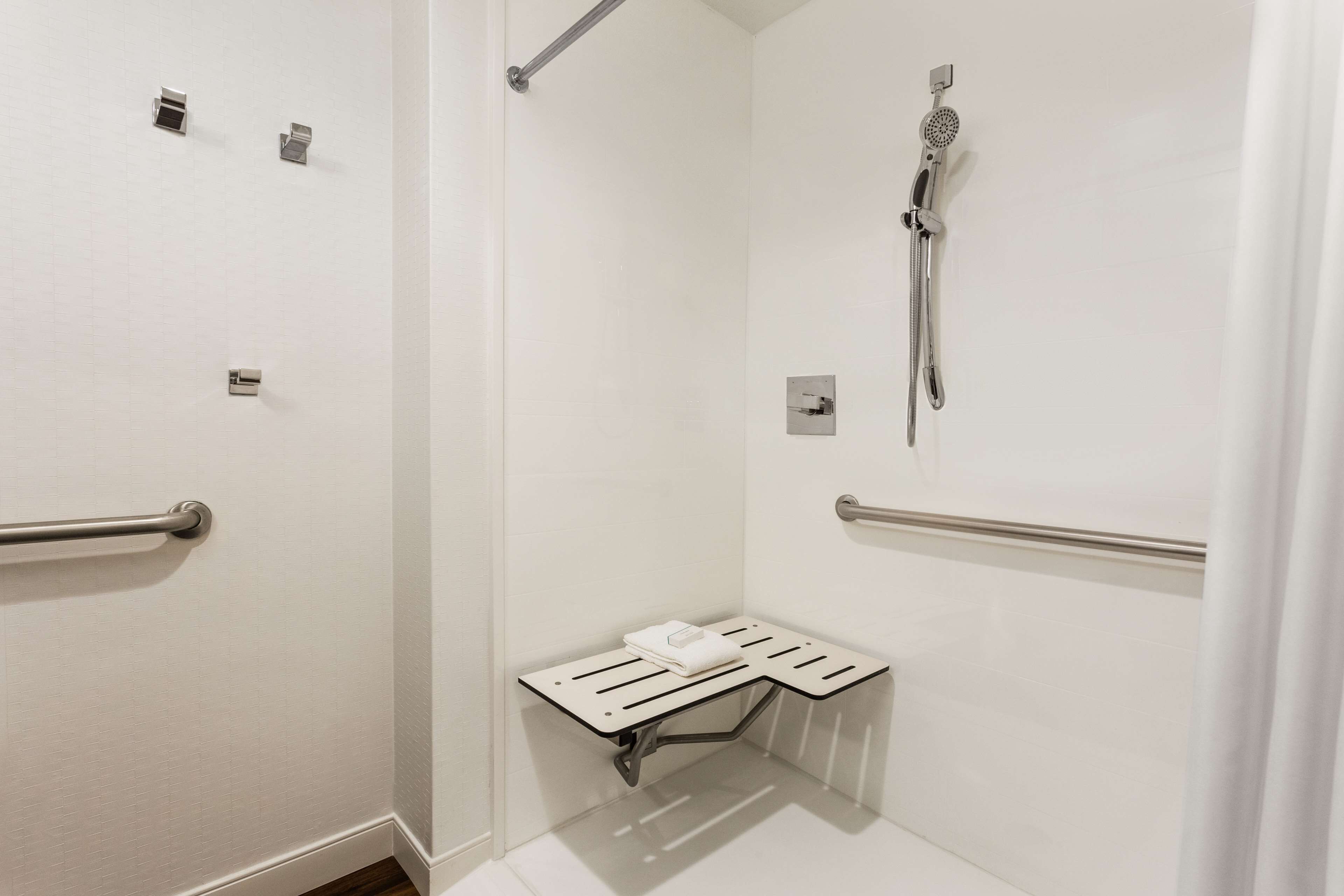 A small, white, walk-in shower with a handheld showerhead, a towel rack, and a grab bar.