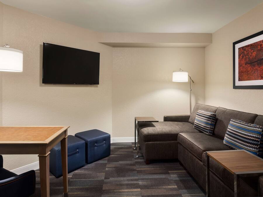 Ein Hotelzimmer mit einem Holztisch, einer Couch, einem Fernseher, einer Lampe und einem gerahmten Bild an der Wand.