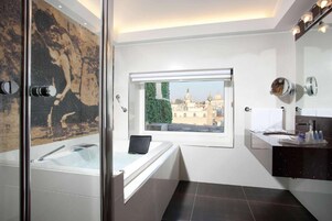 A modern bathroom with a glass-enclosed shower, a bathtub, and a window offering a city view.