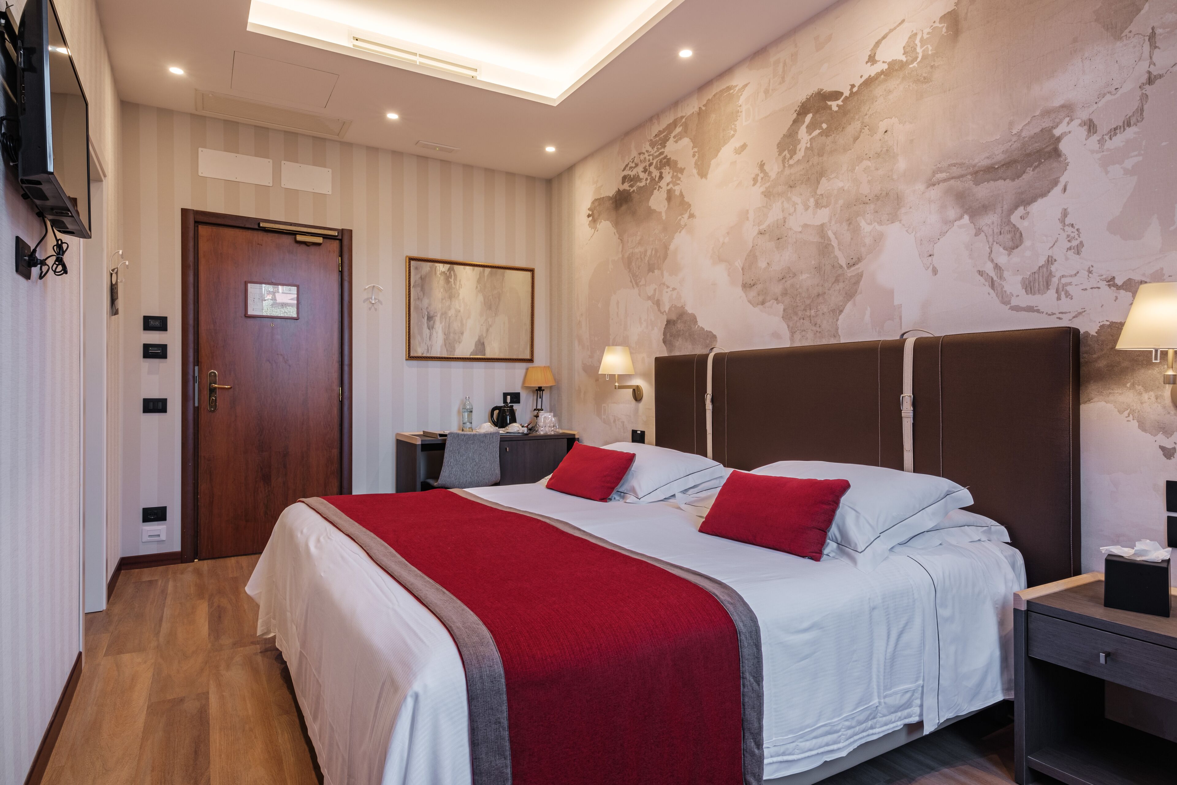 Habitación de hotel con una cama grande, una puerta de madera, un mapa mundial en la pared y un televisor fijado a la pared.