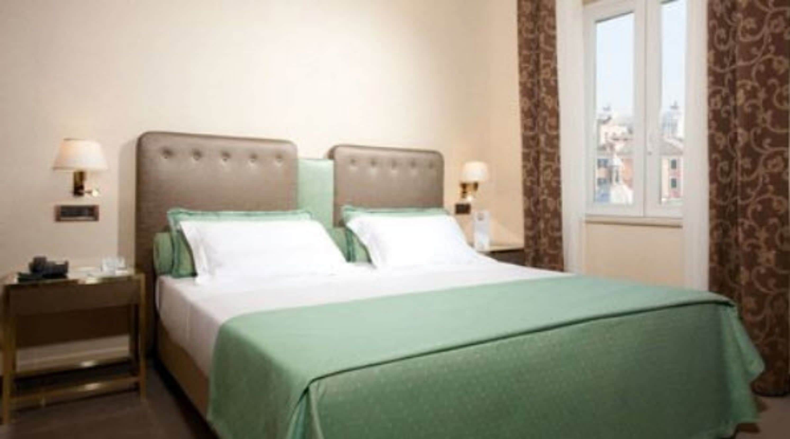 Camera d'albergo con un letto, due comodini e una finestra con vista.