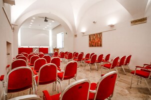 A conference room with rows of red chairs, white walls, and a ceiling projector.