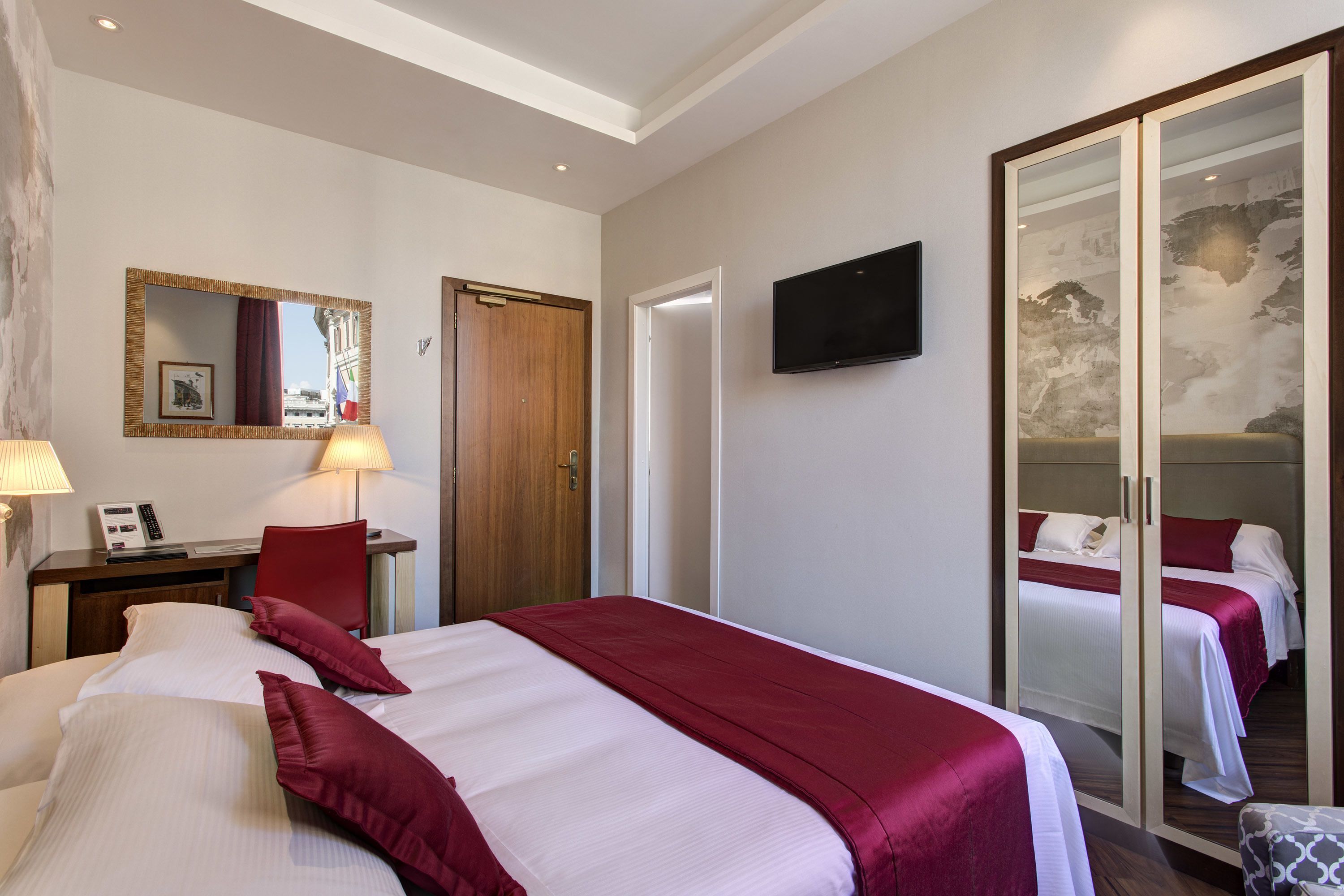 Habitación de hotel con una cama grande, un escritorio con lámpara, televisor y una puerta corrediza que da a otra habitación.