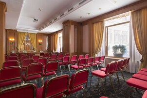 A conference room with rows of red chairs, a podium, and large windows with curtains.