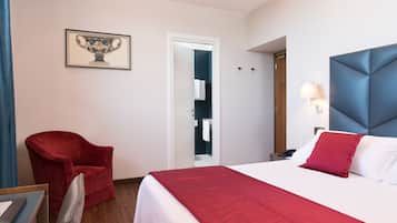 A hotel room with a bed, a red armchair, a framed picture on the wall, and a door leading to a bathroom.