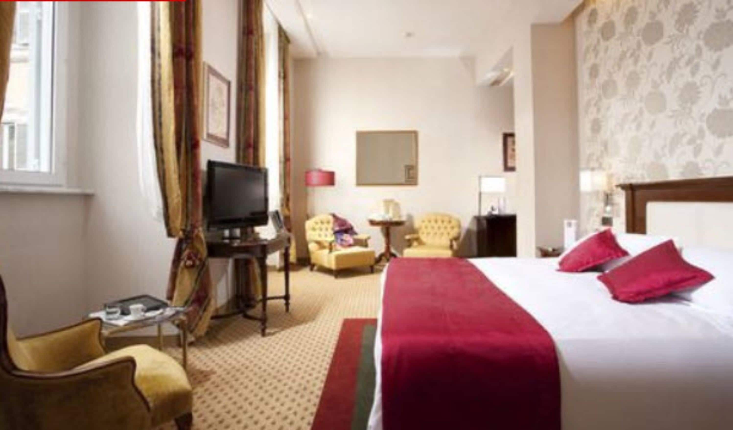Hotelkamer met een groot bed, een televisie, twee fauteuils, een tafeltje en een raam met gordijnen.