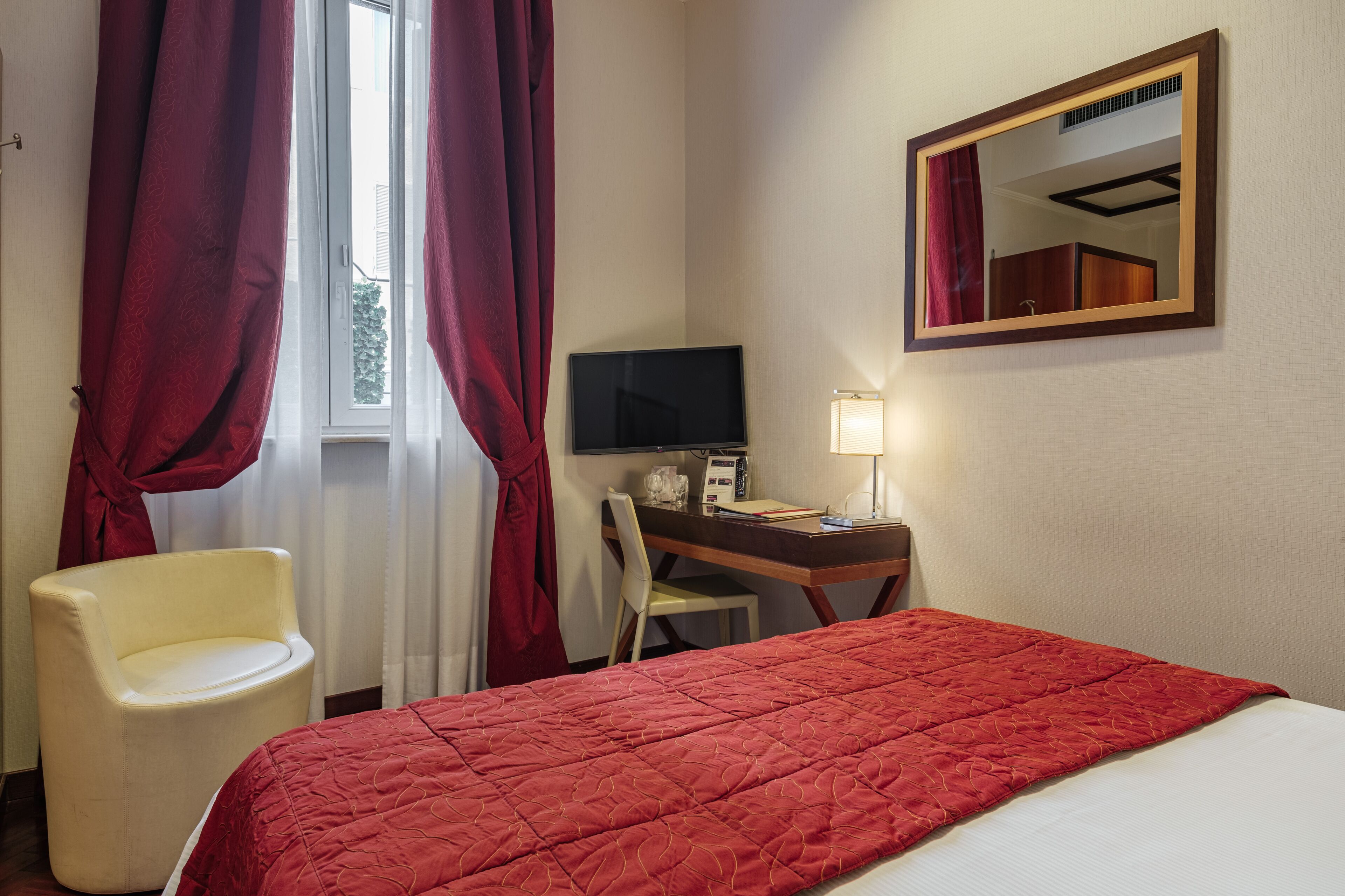 A hotel room with a bed, a desk with a computer, a chair, and a TV.