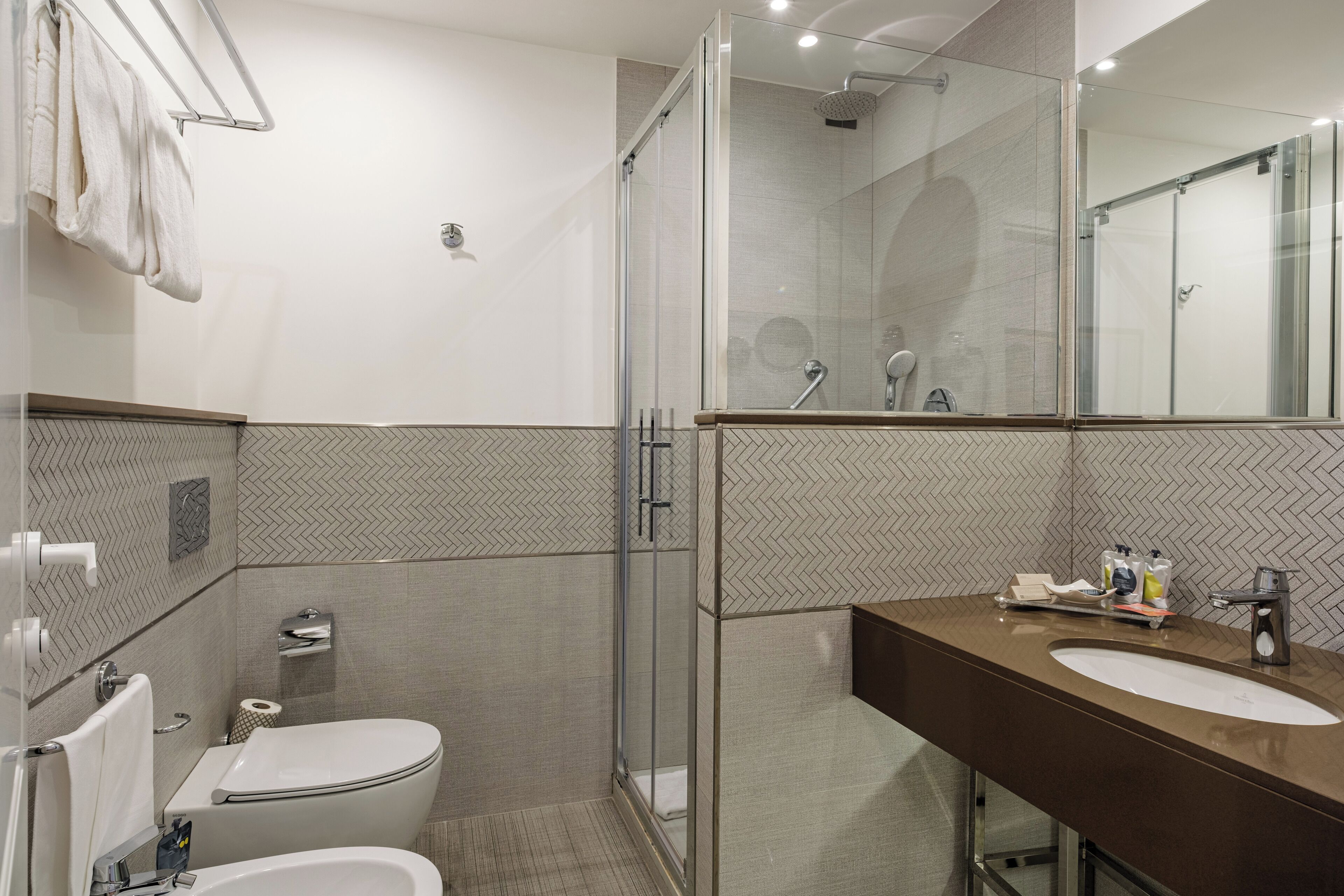 Ein modernes Badezimmer mit einer Duschkabine aus Glas, einer weißen Toilette und einem Waschtisch mit Spiegel.