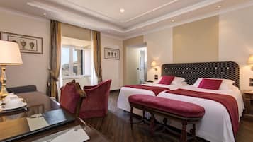 Une chambre d’hôtel avec un plancher en bois, deux lits avec une literie rouge, un bureau avec une lampe et une chaise.