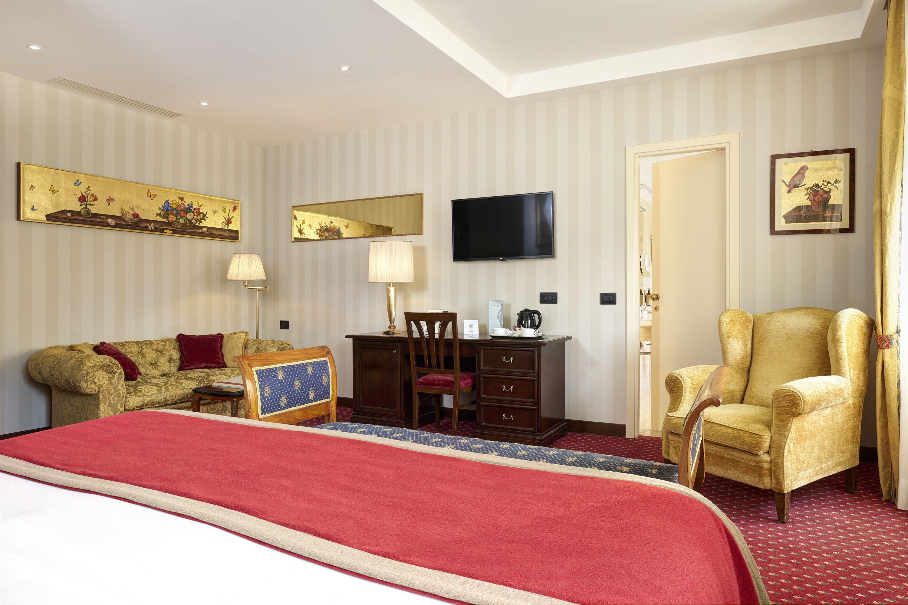 A hotel room with a large bed, a desk with a chair, a television, and a sofa.