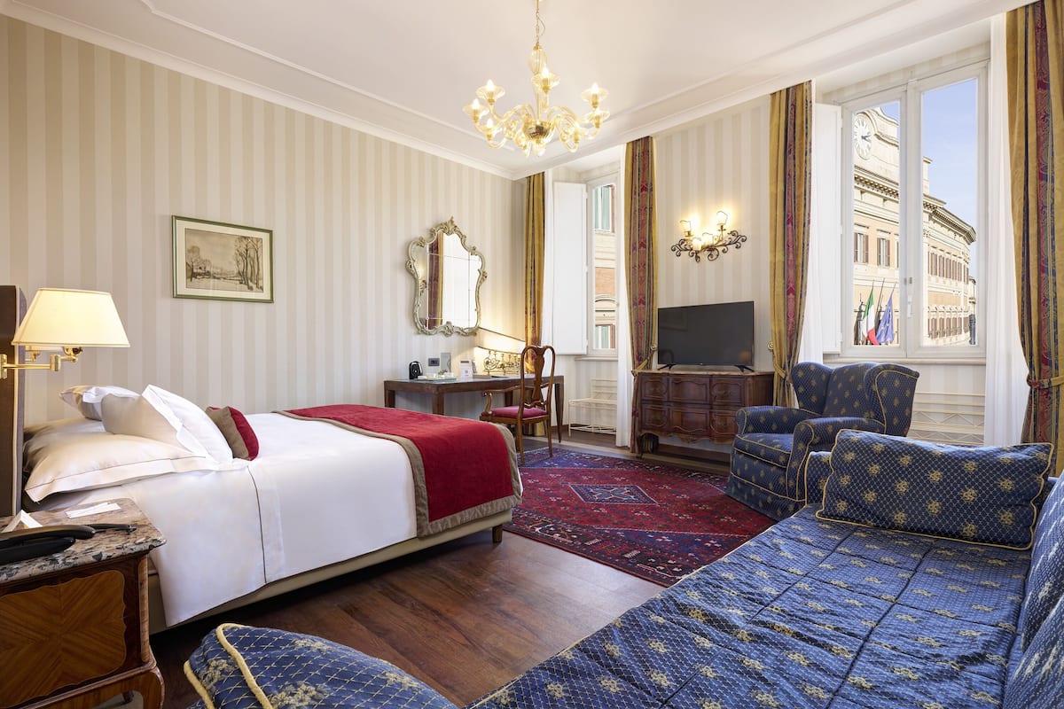 Ett hotellrum med en säng, en soffa, ett skrivbord, en tv och utsikt över staden genom fönstret.