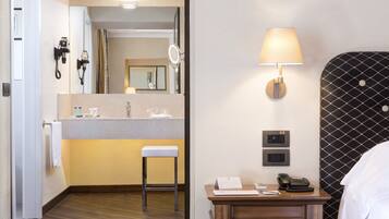 A hotel room with a wooden floor, a small desk with a lamp, a telephone, and a mirror.
