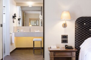 A hotel room with a wooden floor, a small desk with a lamp, a telephone, and a mirror.