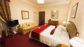 Habitación de hotel con cama, televisor en un soporte, cómoda, espejo y alfombra roja.