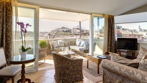 A spacious balcony with a sofa, chairs, and a dining table. A television is mounted on the wall, and a potted plant is on the table. - Hotel Nazionale (Rome)
