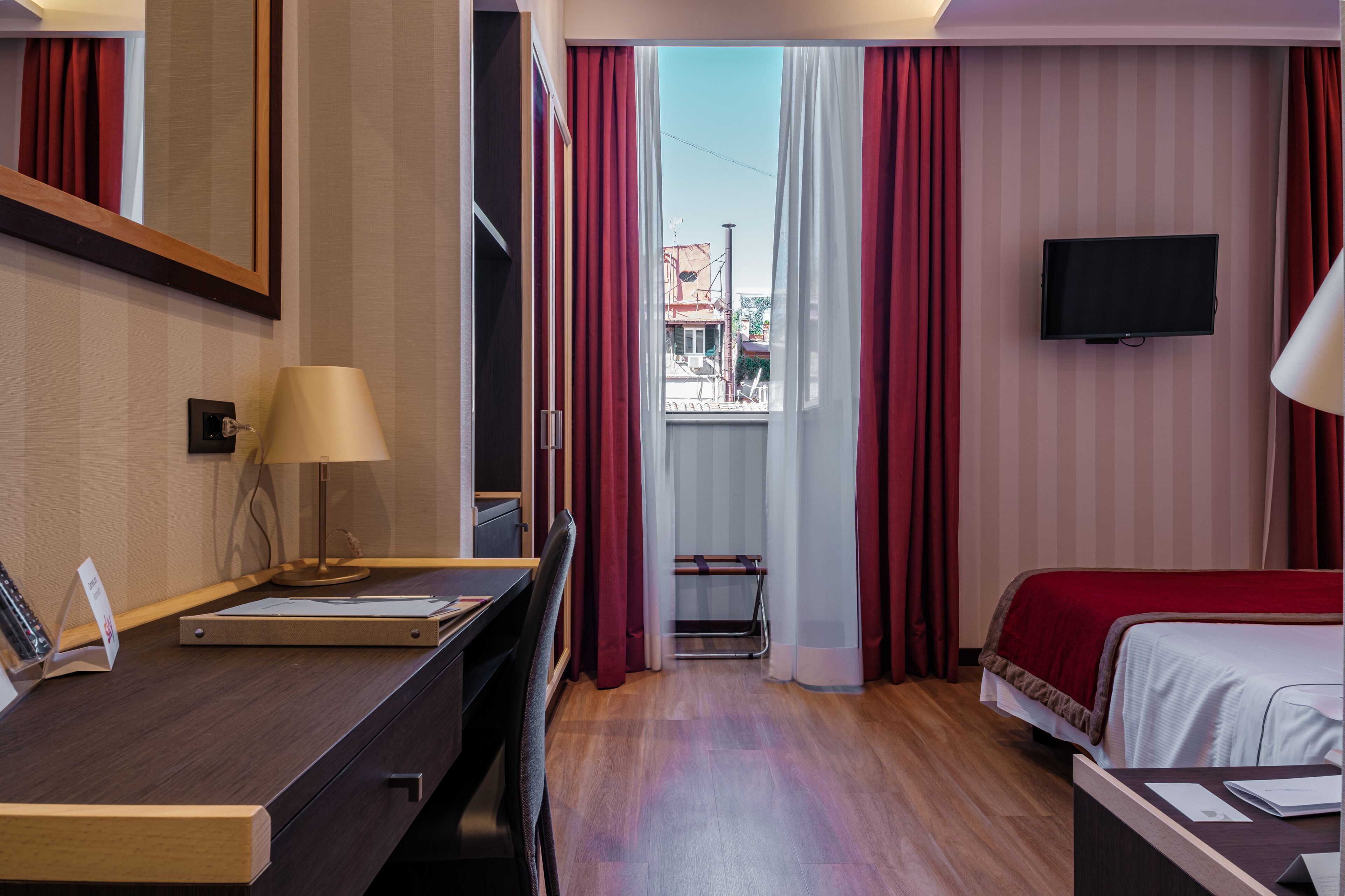 A hotel room with a desk, a bed, a TV, and a window with curtains.