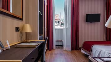 A hotel room with a desk, a bed, a TV, and a window with curtains.
