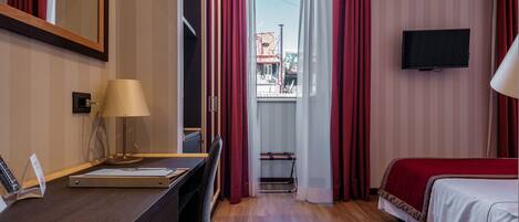 Una habitación de hotel con escritorio, cama, televisión y ventana con cortinas.