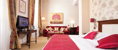 A hotel room with a large bed, a desk with a computer, a red sofa, and a painting on the wall.