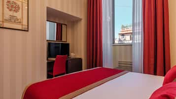 A hotel room with a bed, a desk, a chair, and a large window with red curtains.