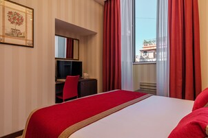 A hotel room with a bed, a desk, a chair, and a large window with red curtains.